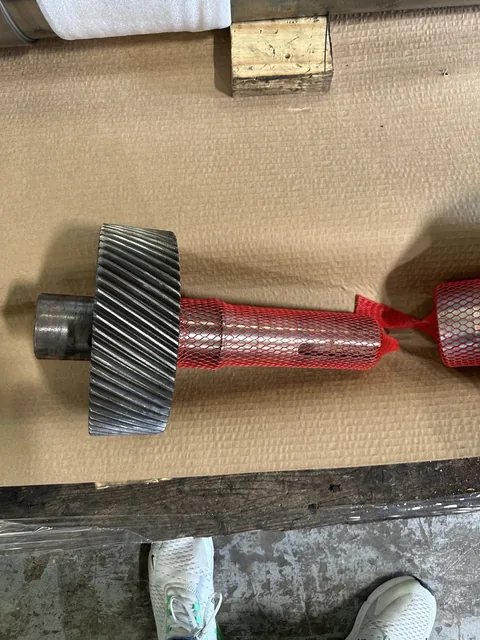 Helical gear-and-shaft component with protective mesh covering part of the shaft.