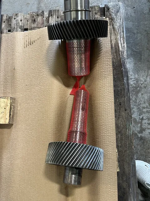 Two helical gear-and-shaft components laid out with protective mesh.