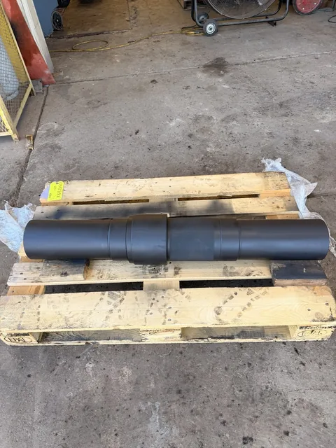 Stepped shaft with a dark surface finish on a pallet; finish type is not identified.