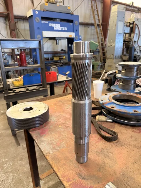 Long helical pinion shaft standing upright on the workbench.