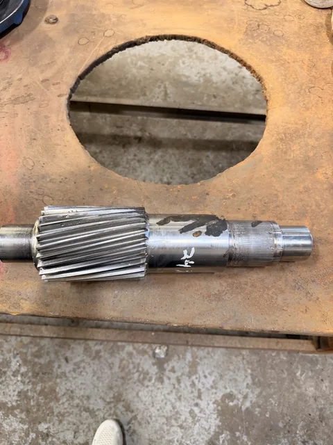 Helical pinion shaft lying horizontally on the workbench.