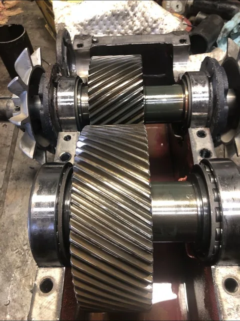 Two helical gears with shafts and bearings installed in an open housing; external cooling fans are visible.